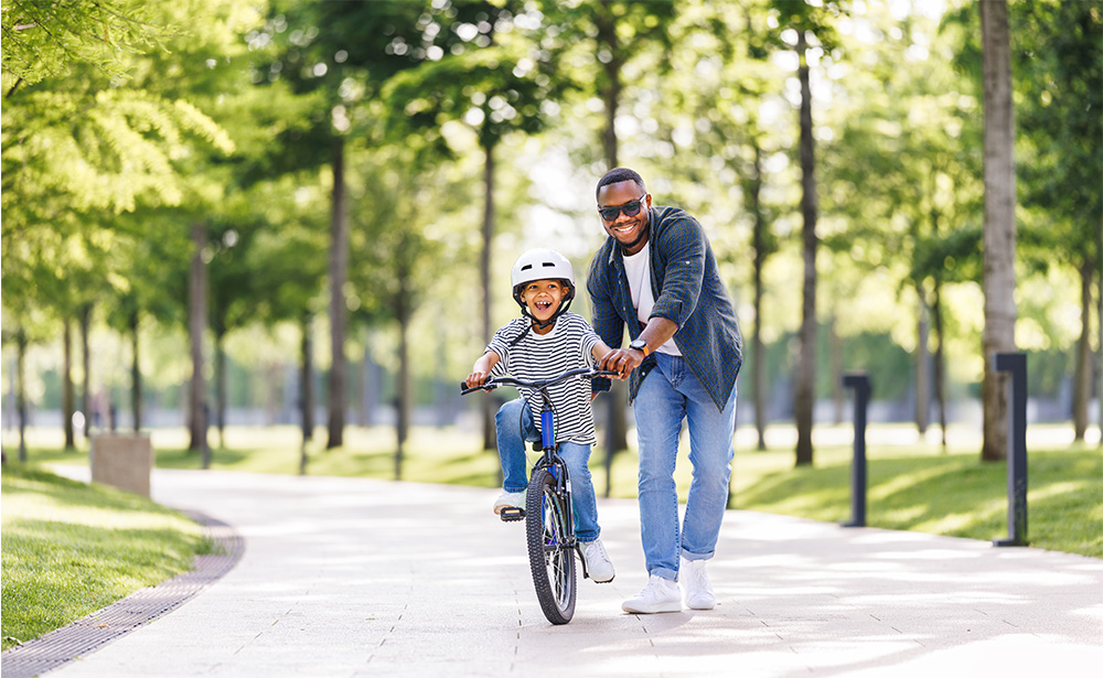 A smiling father helping his son ride a bicycle in a park