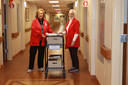 Two Uniontown Hospital volunteers smiling and rolling a cart down the hallway.